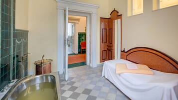 A hotel room with a checkered floor, a bed with a white bedspread, a wooden headboard, a large sink, and a door leading to another room.