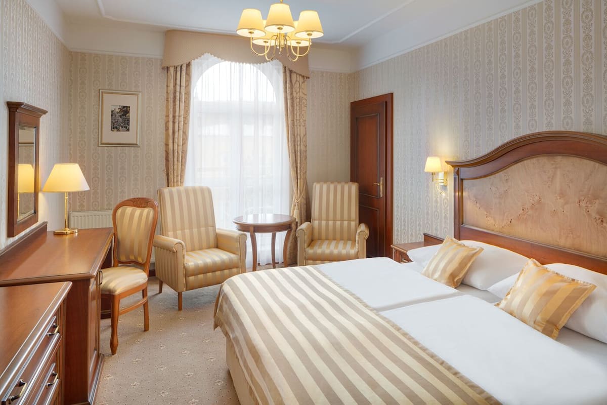 A hotel room with a large bed, two armchairs, a small table, and a desk with a lamp.