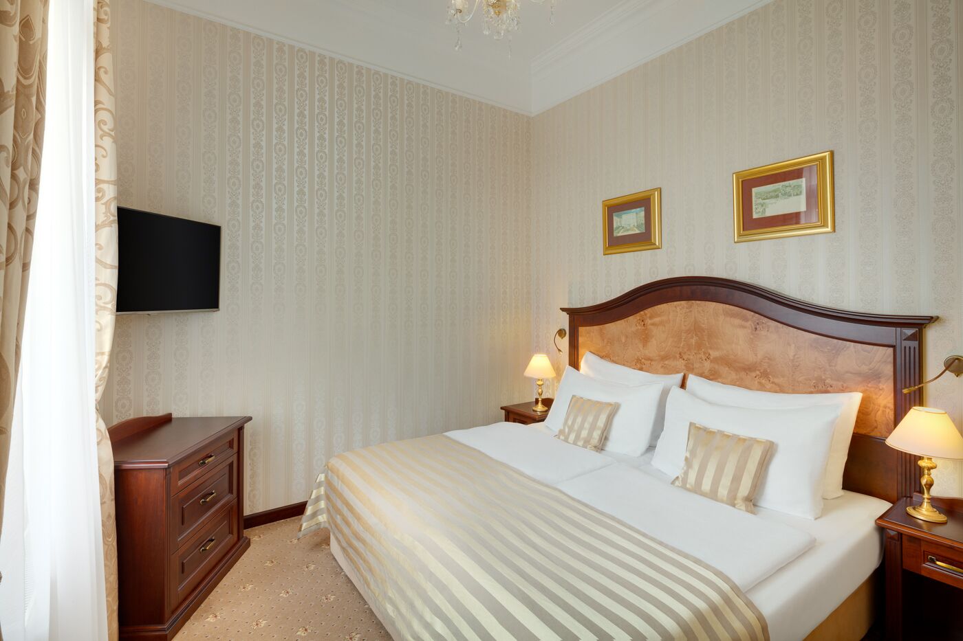 Une chambre d’hôtel avec un grand lit, deux tables de chevet avec des lampes, un téléviseur fixé au mur et une commode en bois.