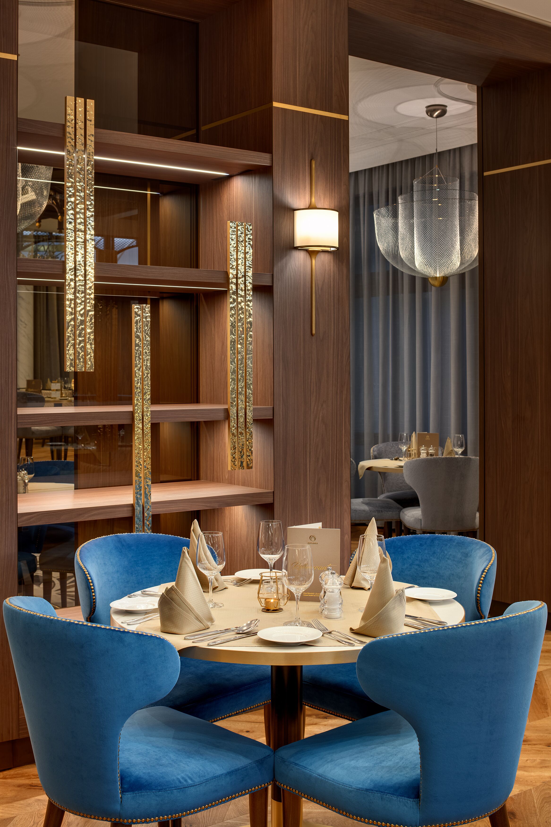 A dining area with a round table, blue upholstered chairs, and a chandelier.