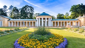A classical building with a central dome, surrounded by a symmetrical garden with yellow and purple flowers.