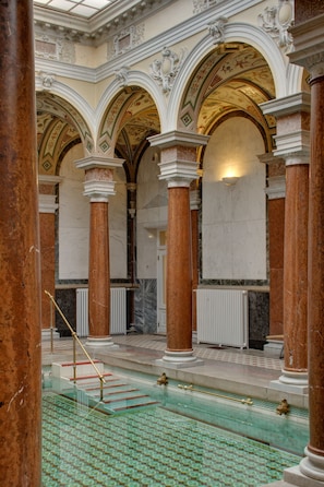A grand hall with marble columns, ornate arches, and a patterned floor.