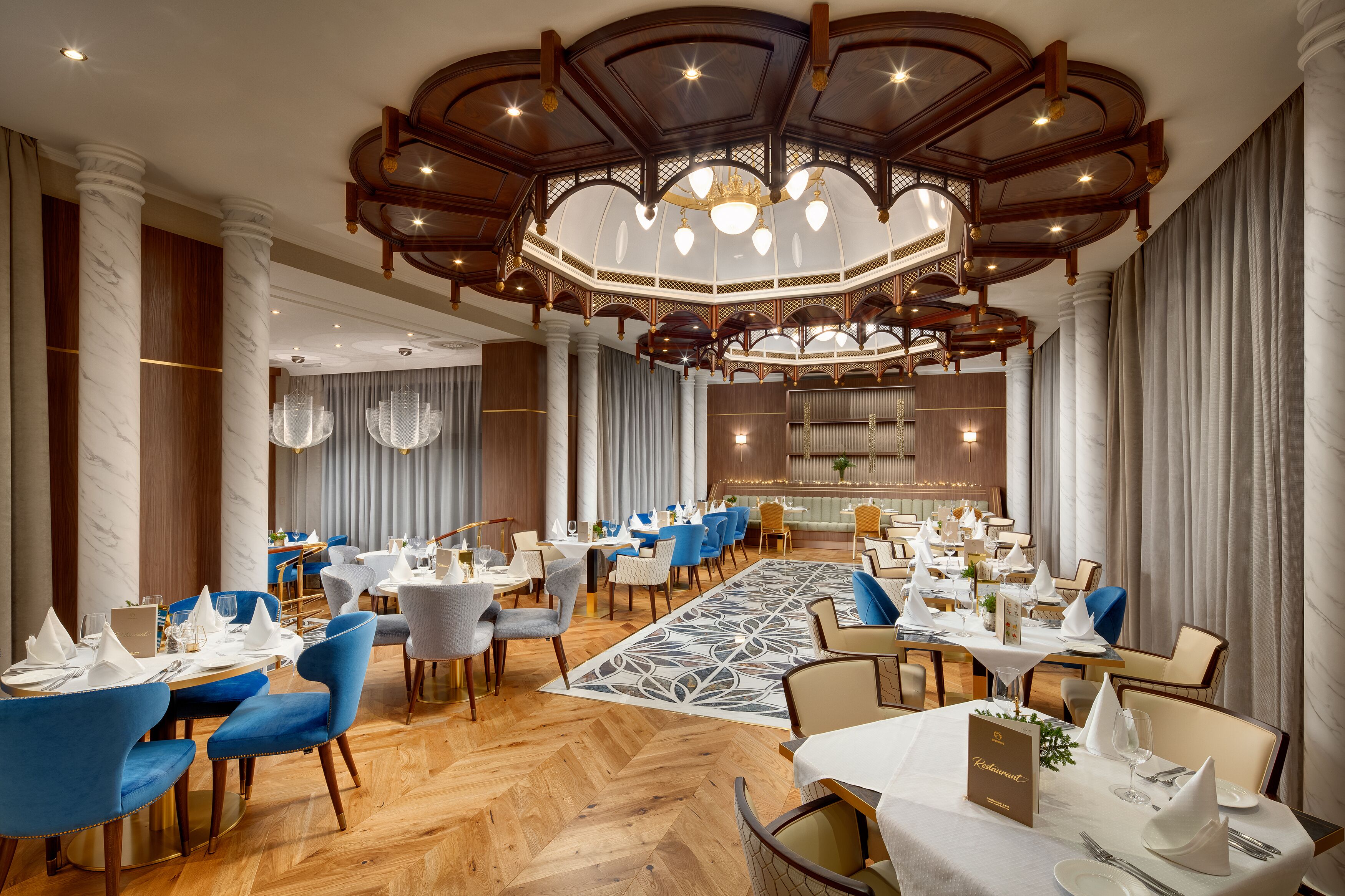 Un vaste espace dédié à la salle à manger, avec plusieurs tables et chaises, une moquette à motifs et un lustre.