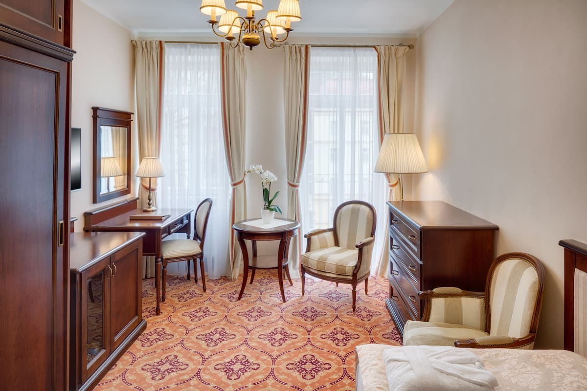 A hotel room with a bed, a desk, two chairs, a dresser, and a chandelier.