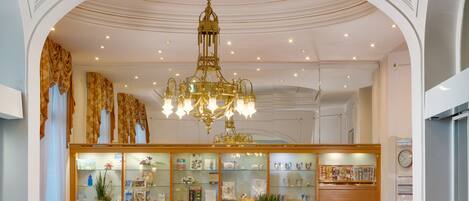 A lobby with a grand chandelier, a reception desk, and a decorative ceiling.