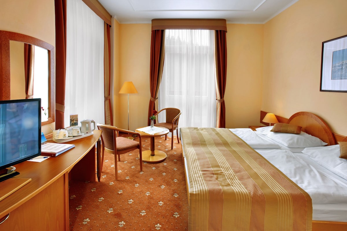 A hotel room with a bed, desk, chair, and a television.