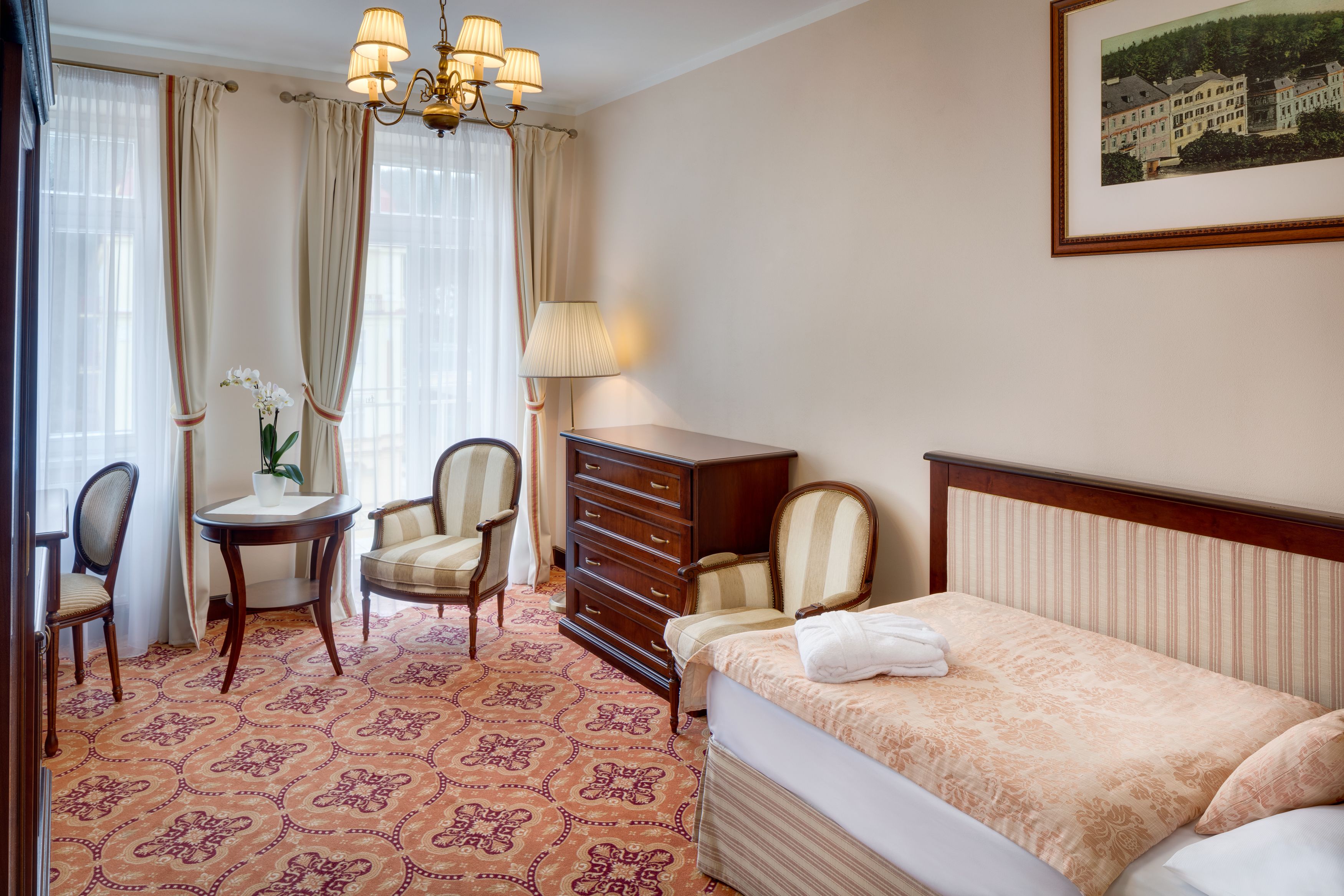 Una habitación de hotel con cama, cómoda, silla, mesa y lámpara.