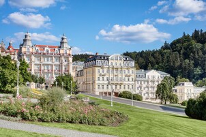Un edificio histórico con arquitectura ornamentada, un jardín bien cuidado y un sendero pavimentado.