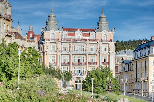 A historic building with ornate architecture, multiple balconies, and a well-maintained garden.