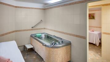 A bathroom with a large bathtub, a small stool, and a table with a pink towel.