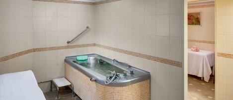 A bathroom with a large bathtub, a small stool, and a table with a pink towel.