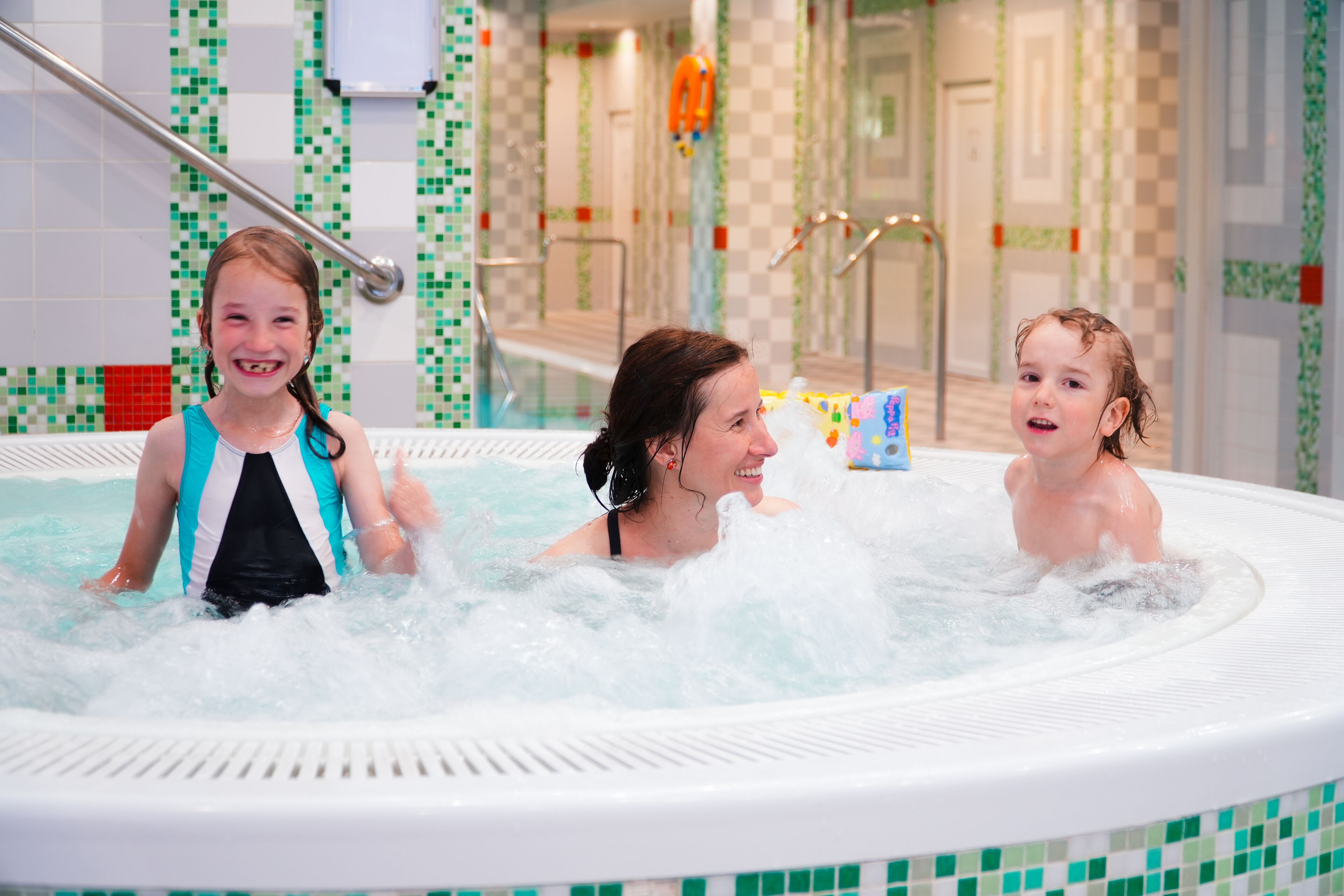 Un jacuzzi con tres personas, rodeado de paredes de azulejos con un diseño a cuadros.