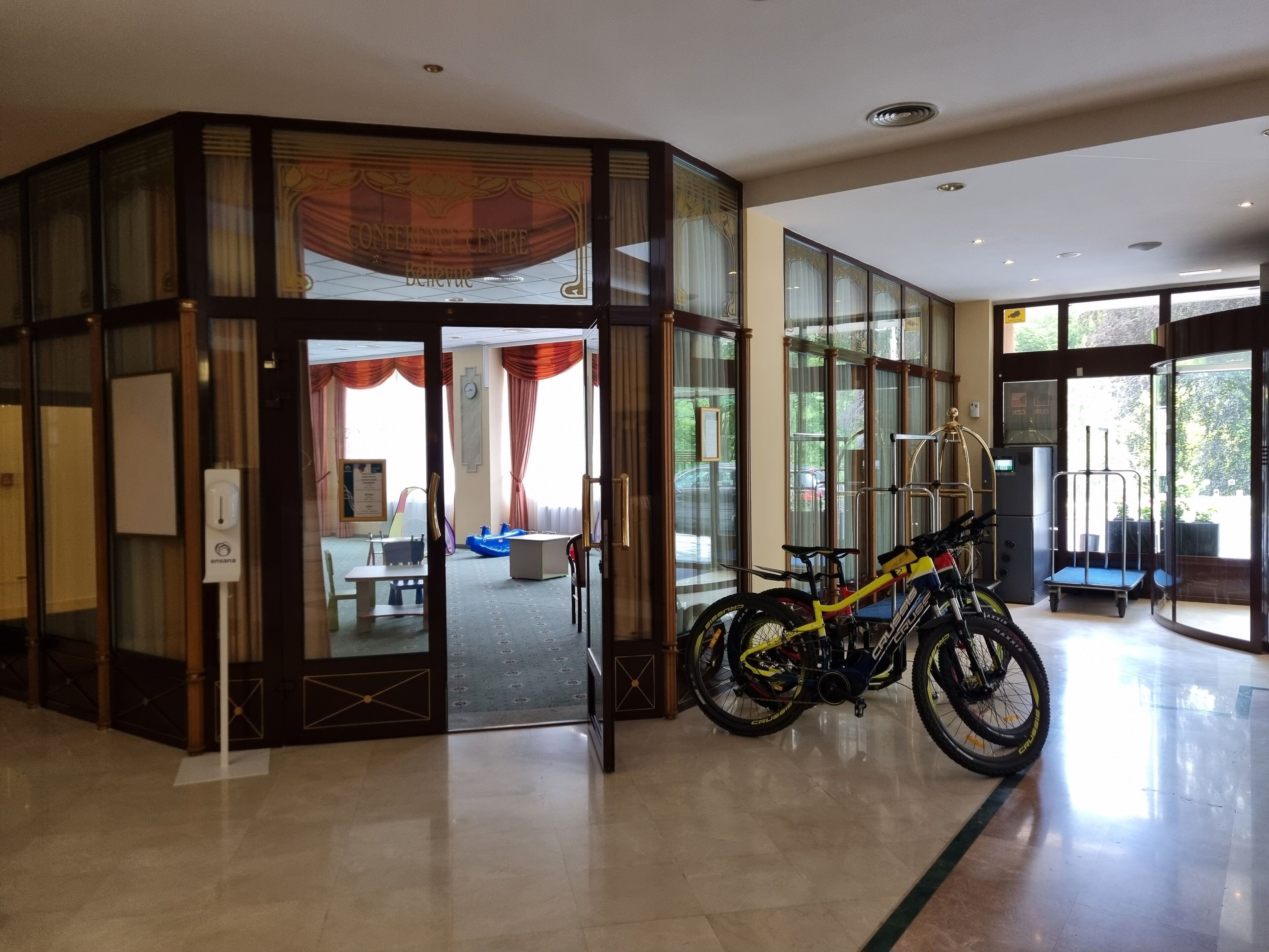 A hotel lobby with a glass door entrance, a bicycle, and a seating area with a table and chairs.