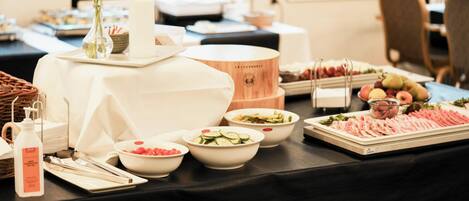 A buffet table with various food items, including sliced cucumbers, tomatoes, and meats, along with a candle and a vase with flowers.