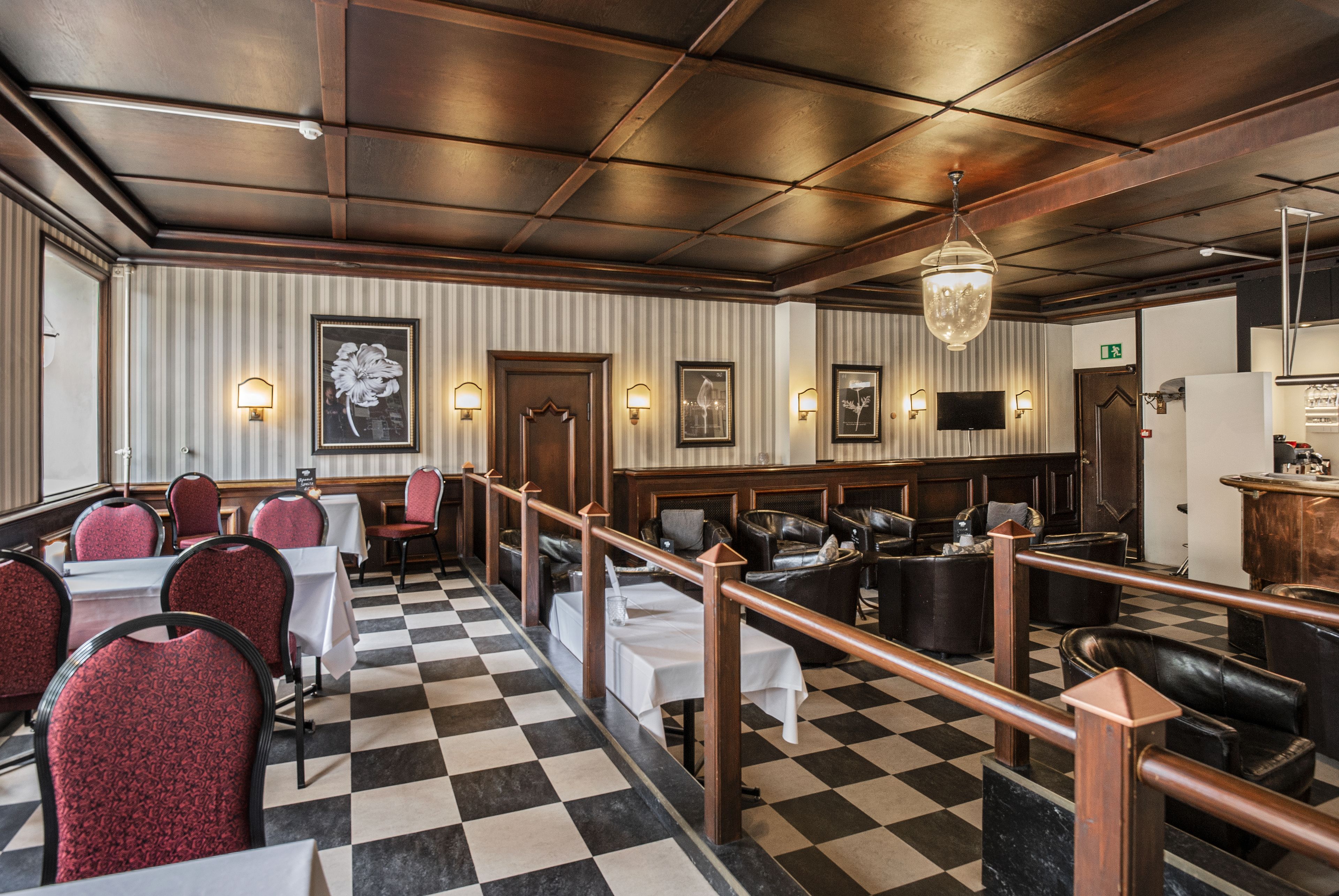 Een restaurant met een zwart-witte vloer, rode bekleden stoelen en een houten plafond.
