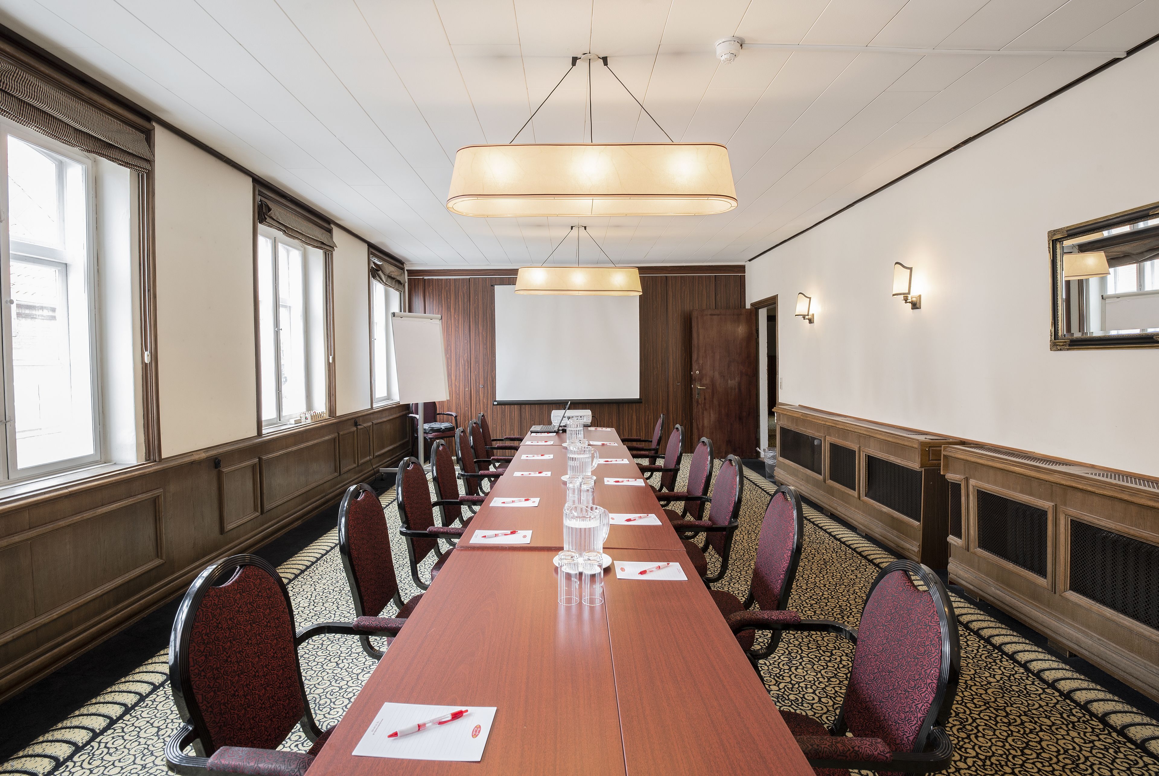 Une salle de conférence avec une longue table, des chaises, un écran de projection et une grande fenêtre.