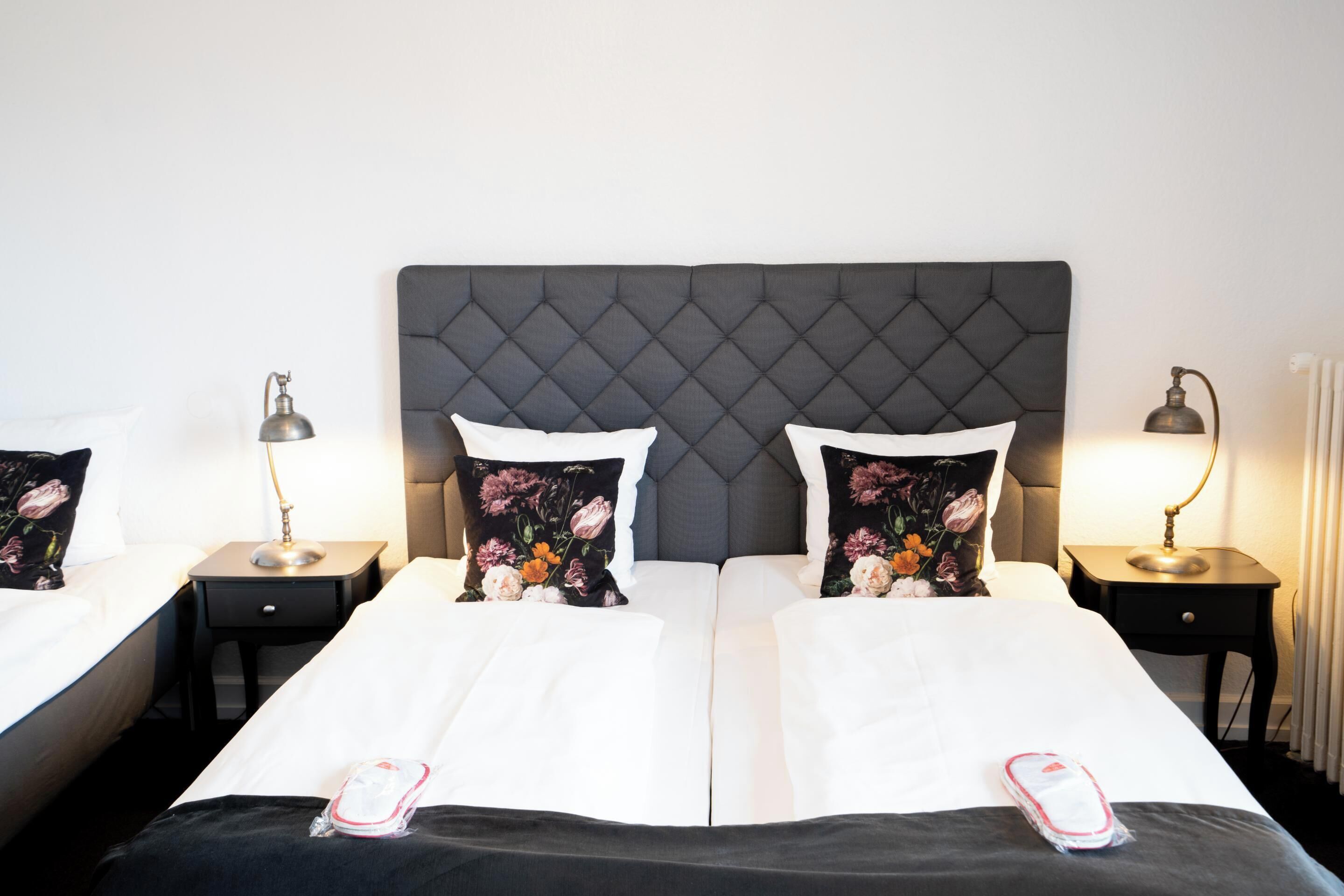Una cama doble con cabecera capitonada, dos mesitas de noche con lámparas y almohadas estampadas con motivos florales.