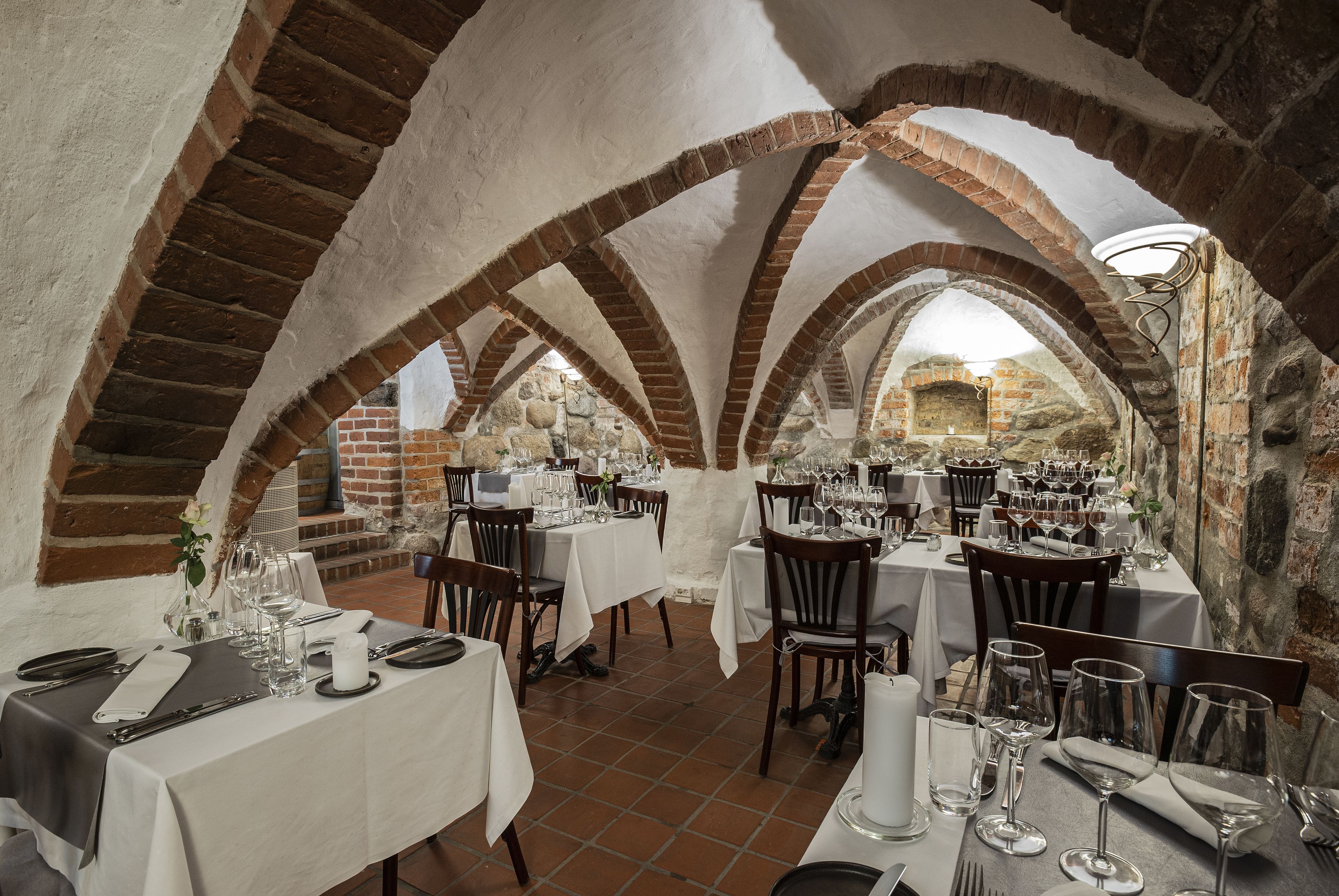 Un comedor interior con arcos de ladrillo, manteles blancos y mesas dispuestas con cuidado.