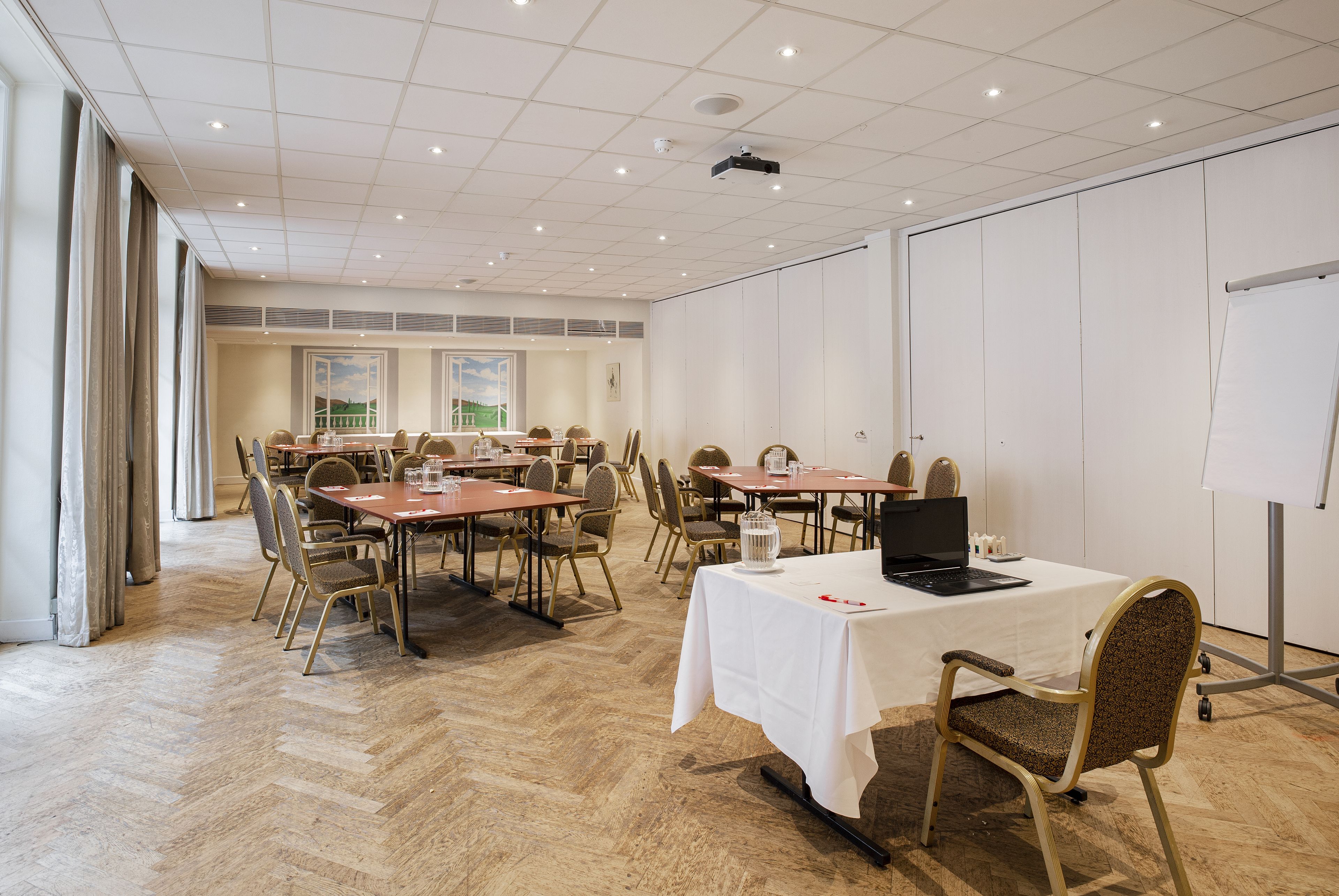 Un salón de conferencias con varias mesas y sillas, una pizarra y un proyector en el techo.