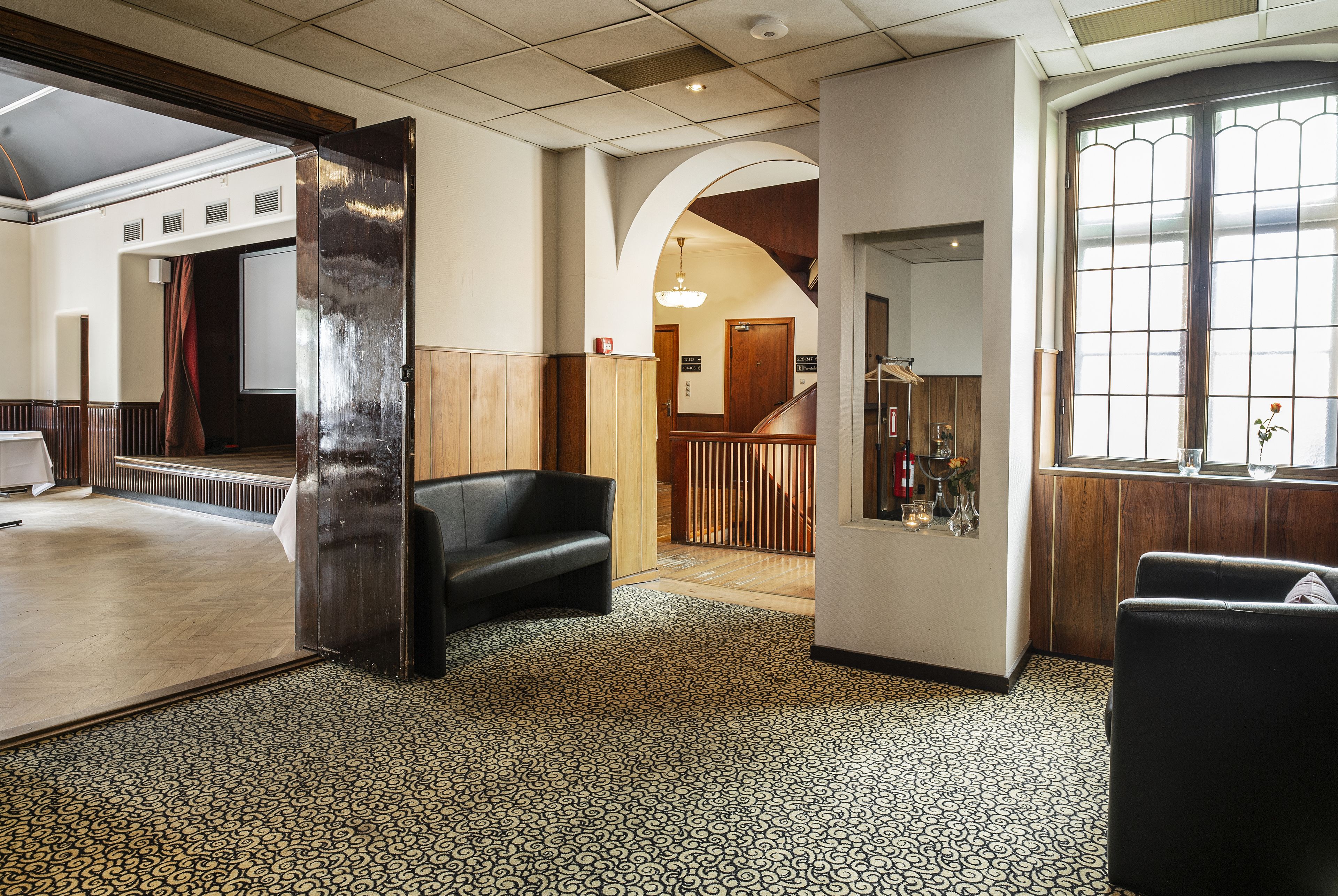 A spacious lobby with patterned flooring, a staircase, and a reception area with a counter and decorative items.