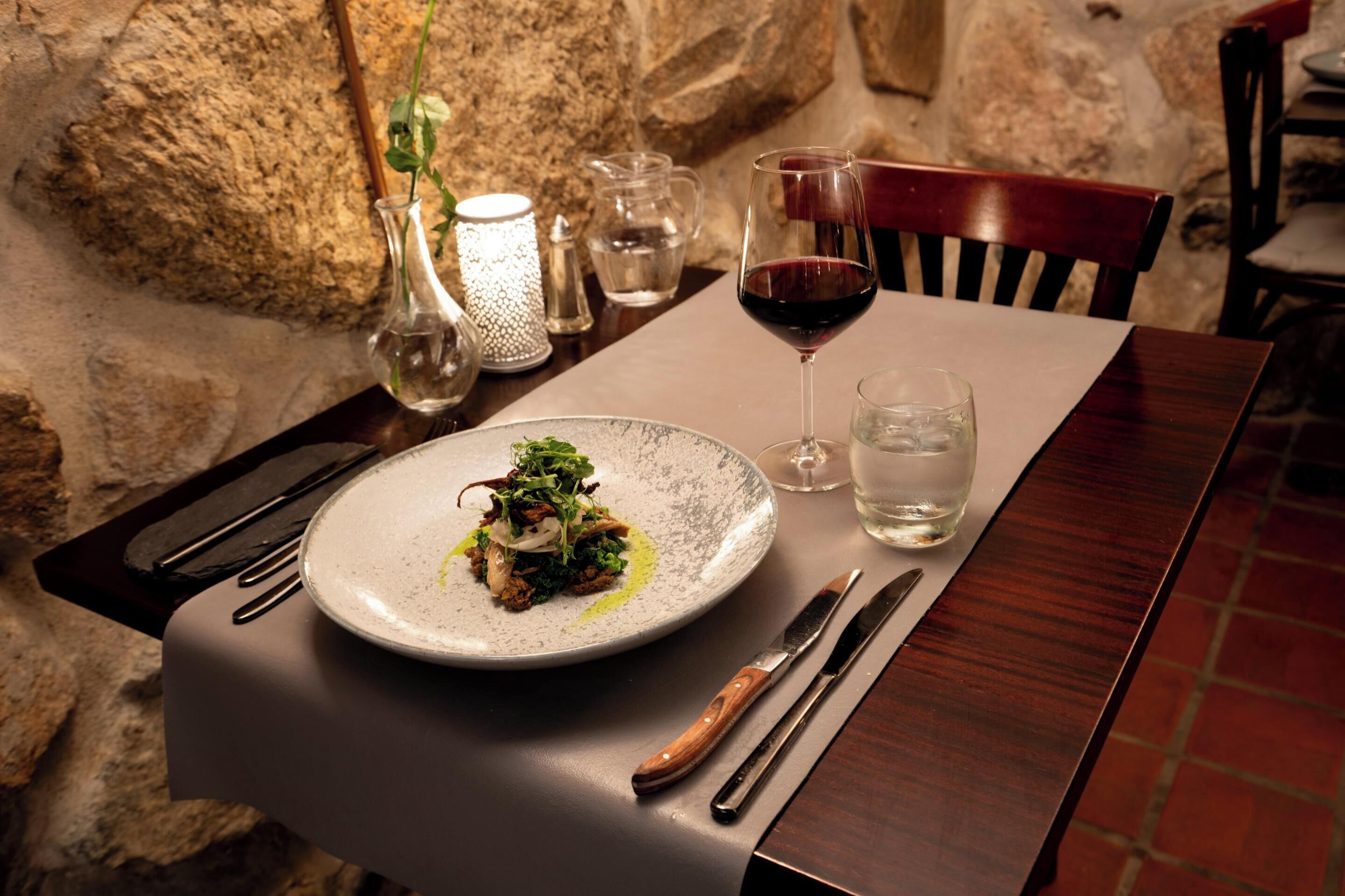 A dining table set with a plate of food, a glass of red wine, and a water glass.