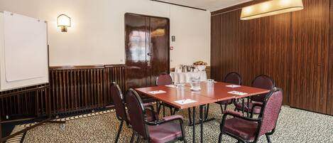 A conference room with a large table, six chairs, a whiteboard, and a wooden panel wall.