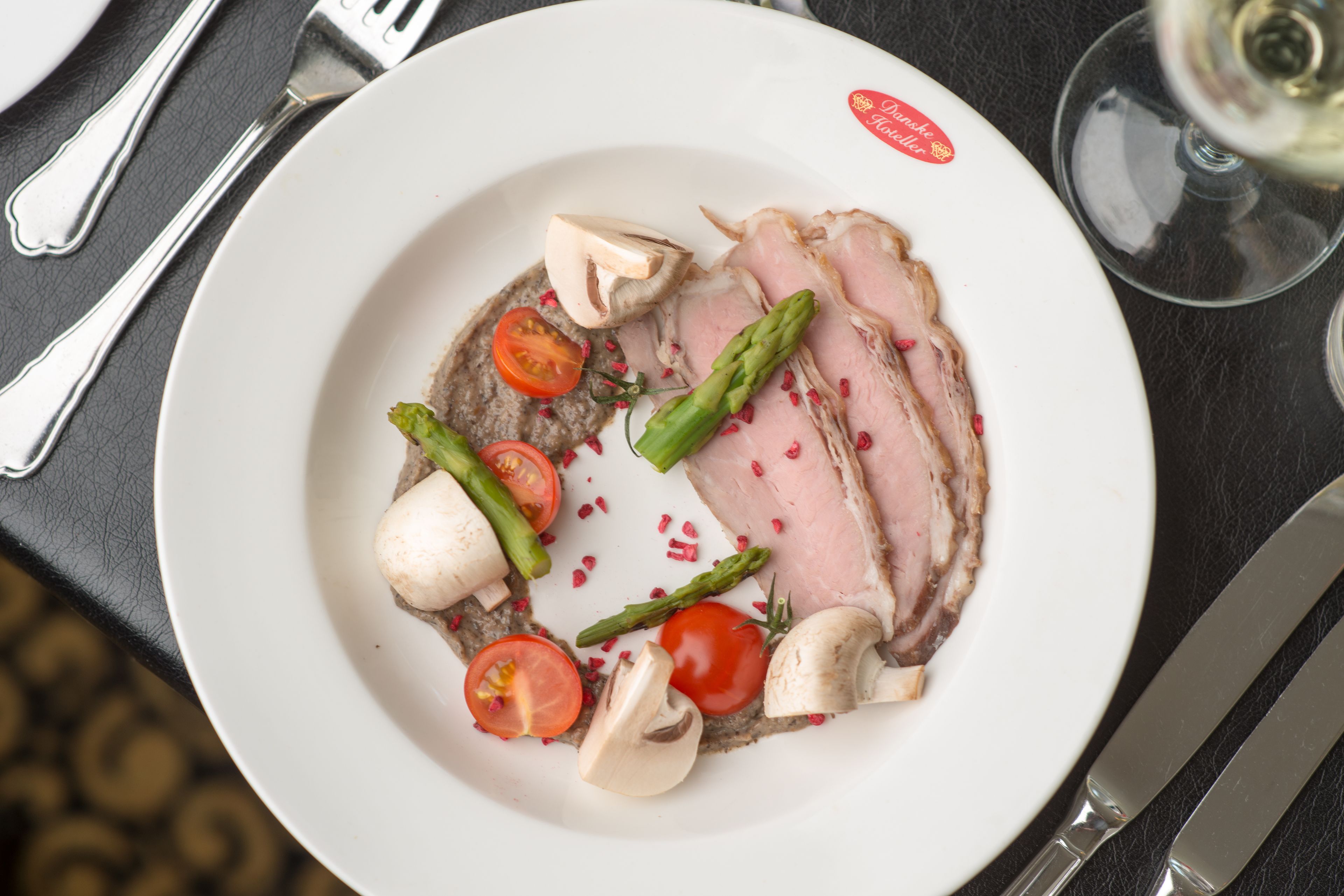 A plate of sliced meat with vegetables on a white plate.