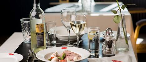 A dining table set with a bottle of St. Regis Chardonnay, wine glasses, a rose, and a plate of food.