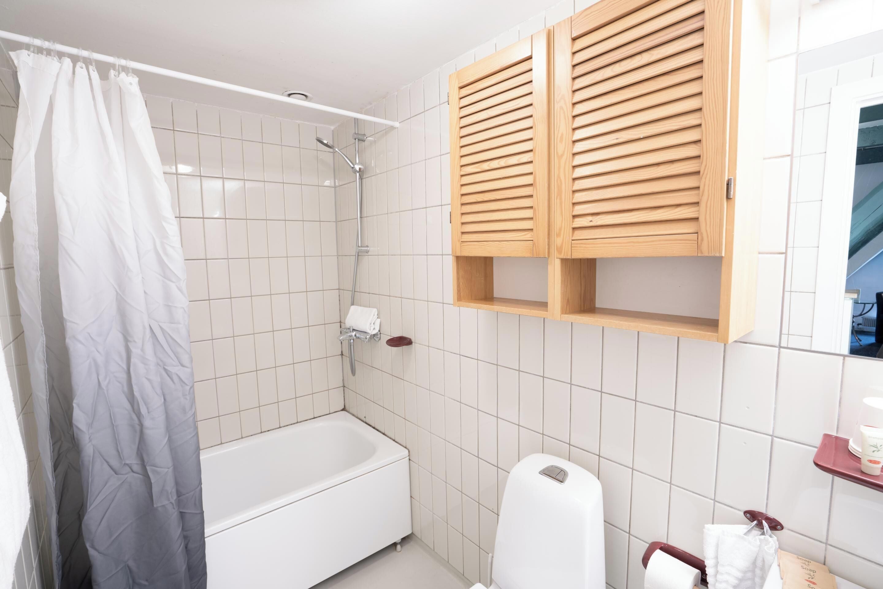 A bathroom with a bathtub, a shower, and wooden cabinets above the sink.