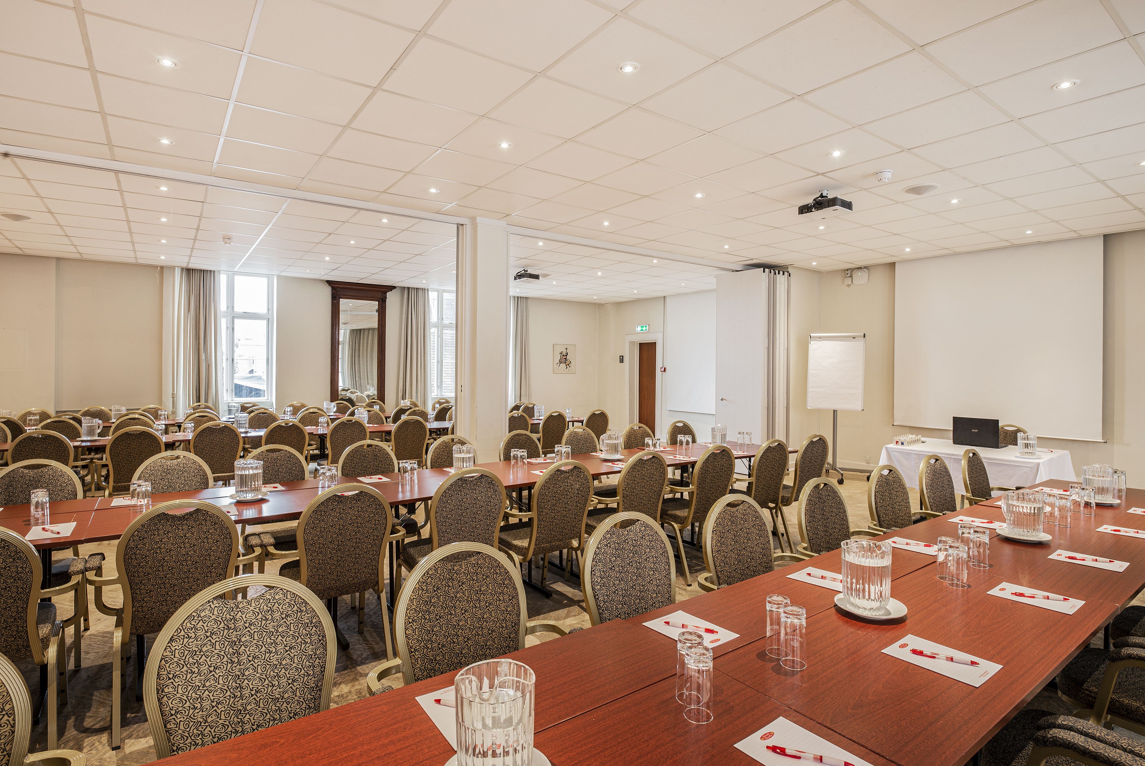 A conference room with multiple tables and chairs, equipped with projectors and a whiteboard.