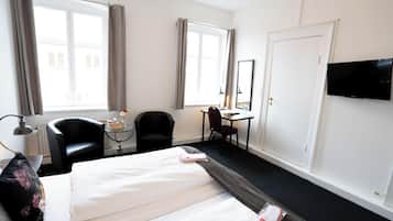 A hotel room with two beds, a desk, a chair, a TV, and a window with curtains.