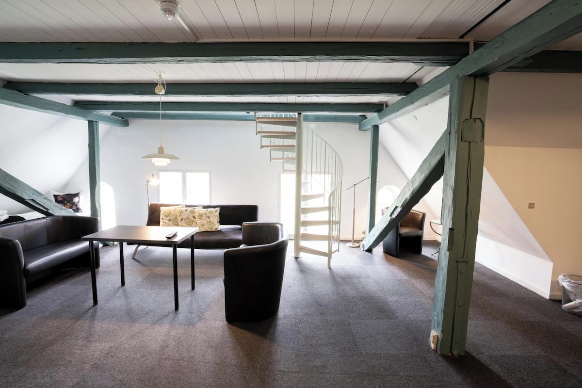Un loft amplio con vigas de madera a la vista, una escalera y un rincón de descanso acogedor con un sofá y sillones.