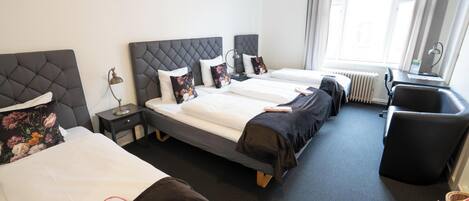 A hotel room with two beds, a desk, a chair, and a window.