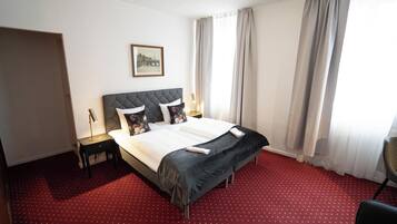 A hotel room with a large bed, a nightstand, a lamp, and a chair.