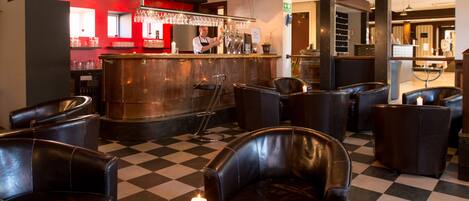 A bar area with leather chairs, a checkered floor, and a bar counter with a red backdrop.