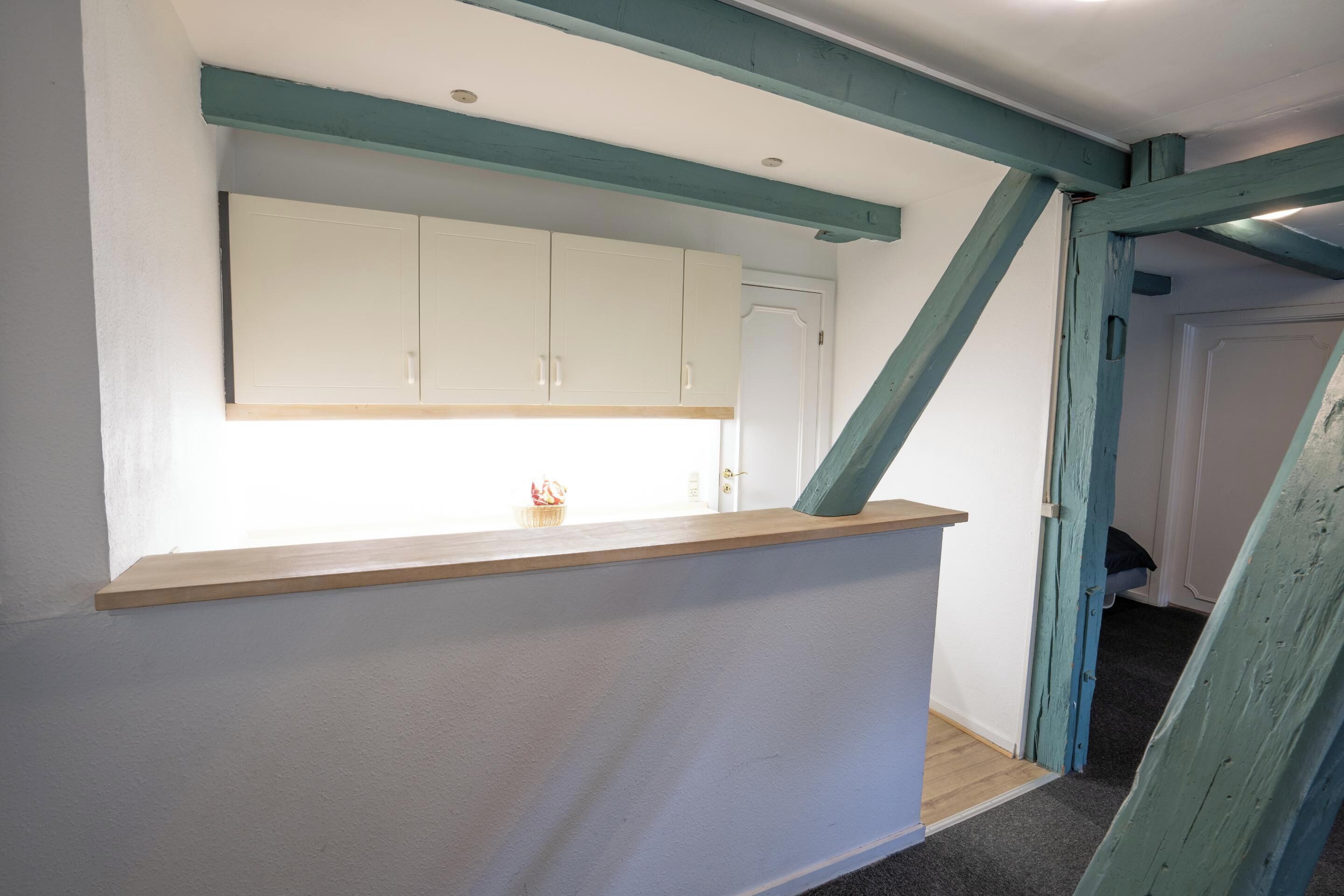 A room with a kitchen area featuring white cabinets, a wooden countertop, and teal painted beams.