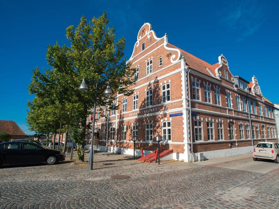 Un edificio histórico con fachada de ladrillo rojo, amplias ventanas y una destacada torre del reloj.