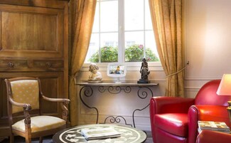 A room with a wooden cabinet, a red leather chair, a round table with a book, and a window with curtains.