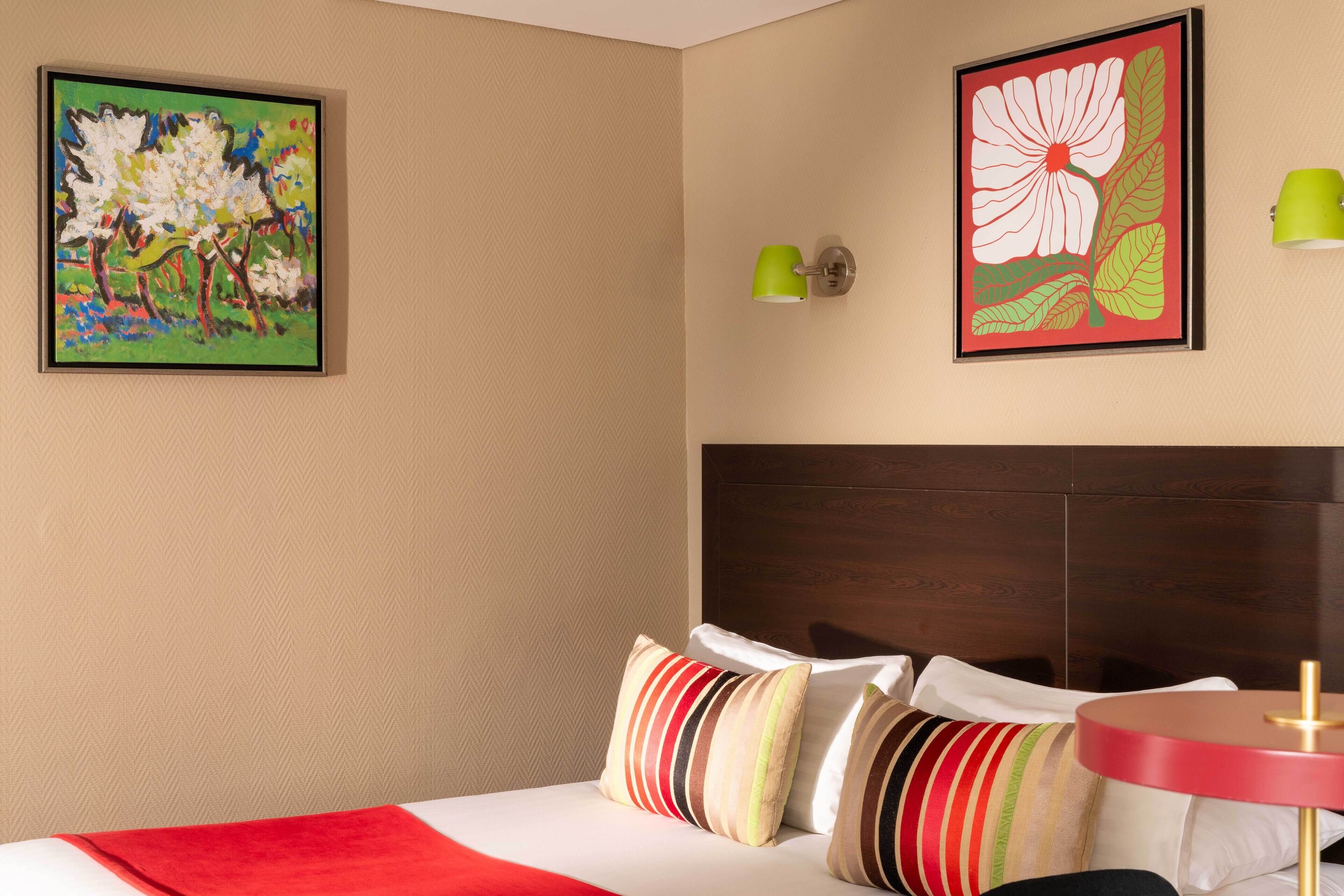 A hotel room with a bed, pillows, a round table, and two wall-mounted lamps.