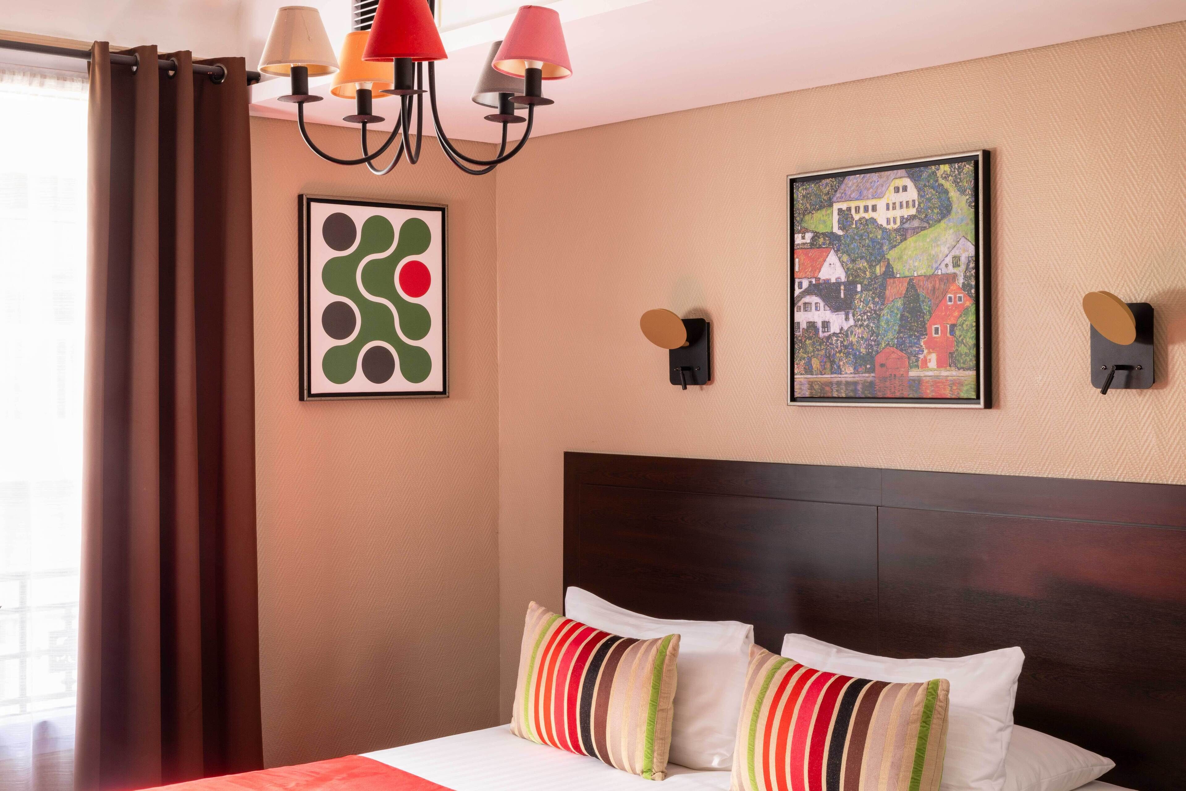 Una habitación de hotel con cama, cortinas, una araña y dos lámparas de pared.