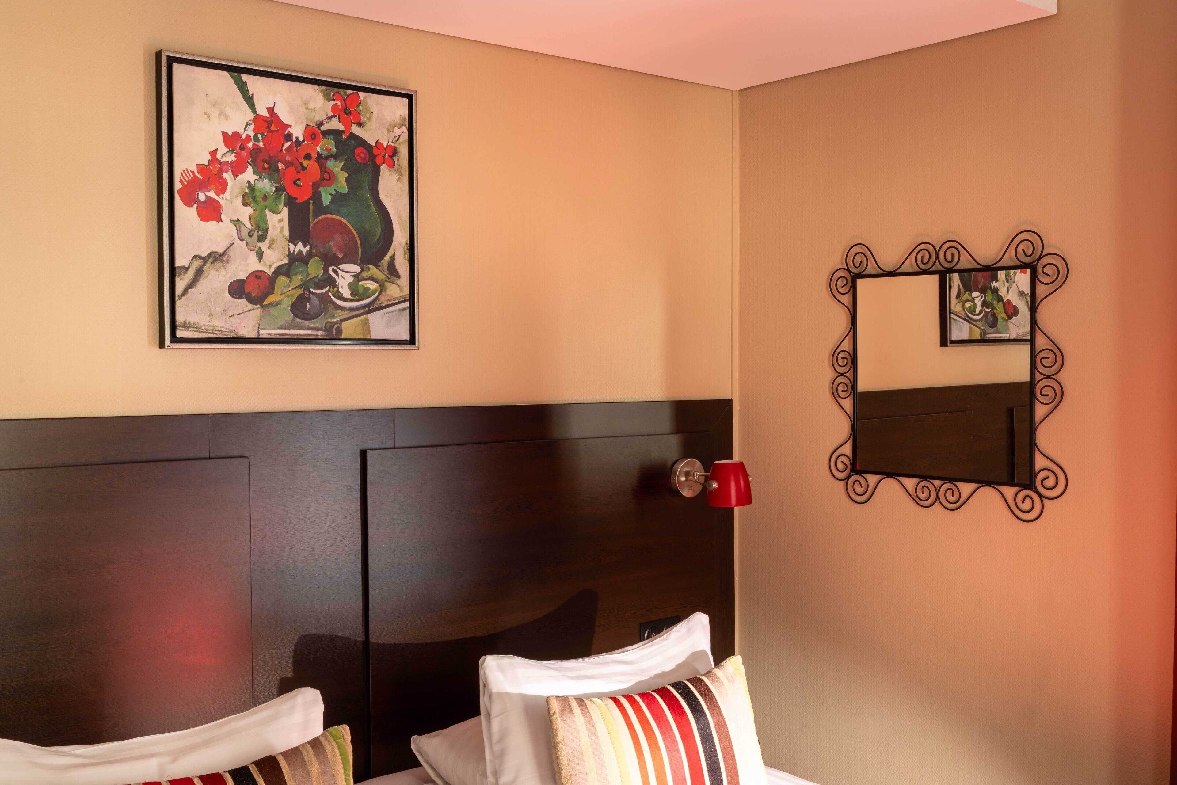 A hotel room with a bed, a headboard, a wall-mounted mirror, and a painting.