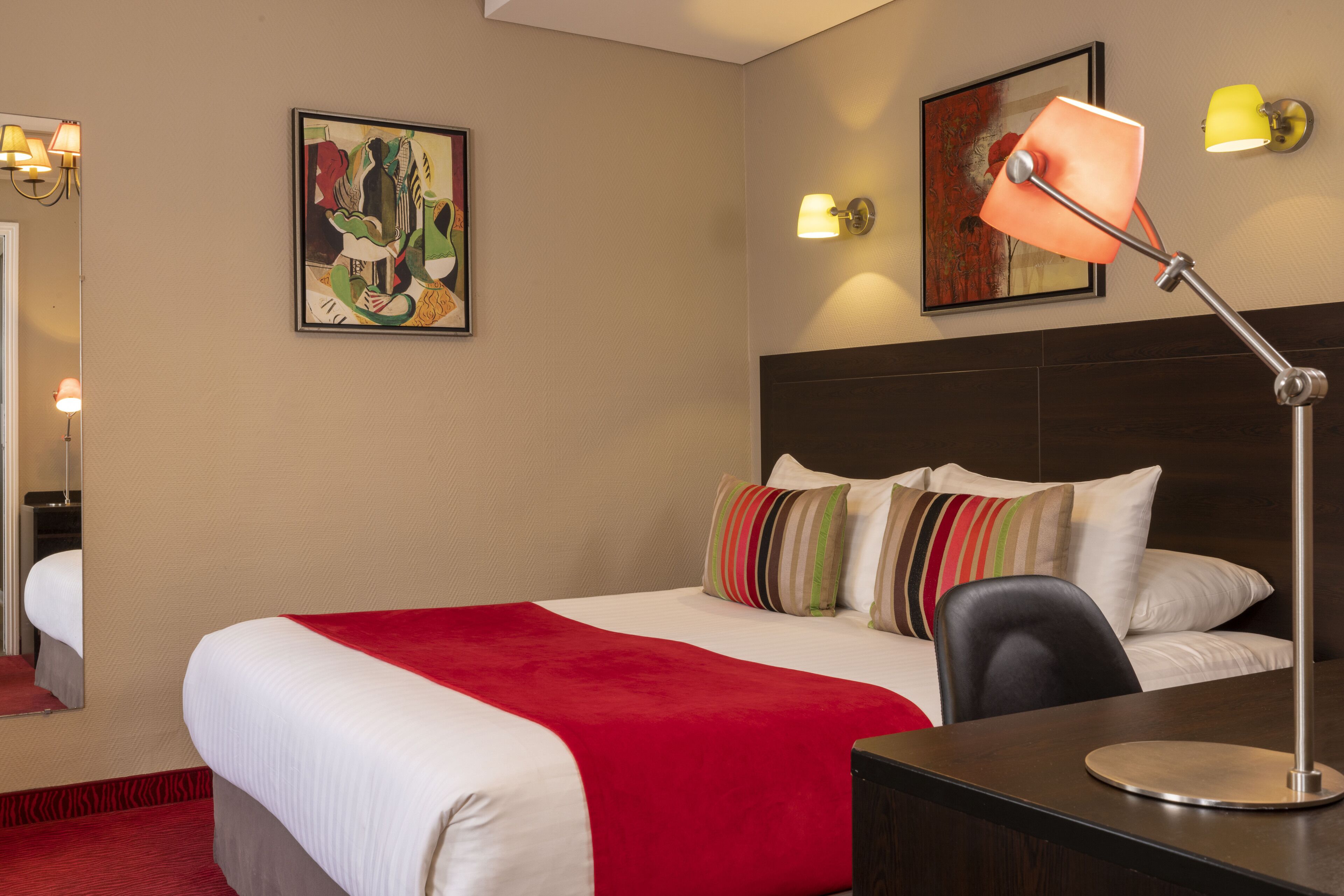Ett hotellrum med en stor säng, ett skrivbord med en lampa och två väggmonterade lampor.