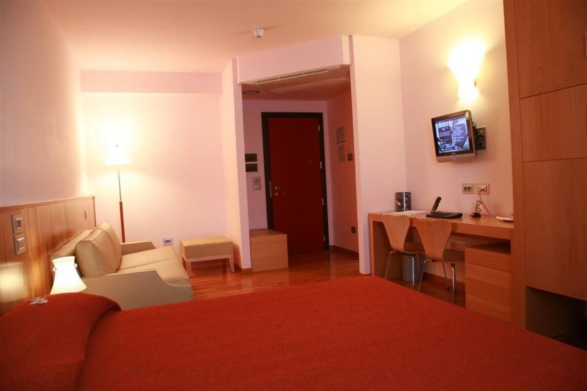 A hotel room with a bed, a desk, a chair, a lamp, and a television.