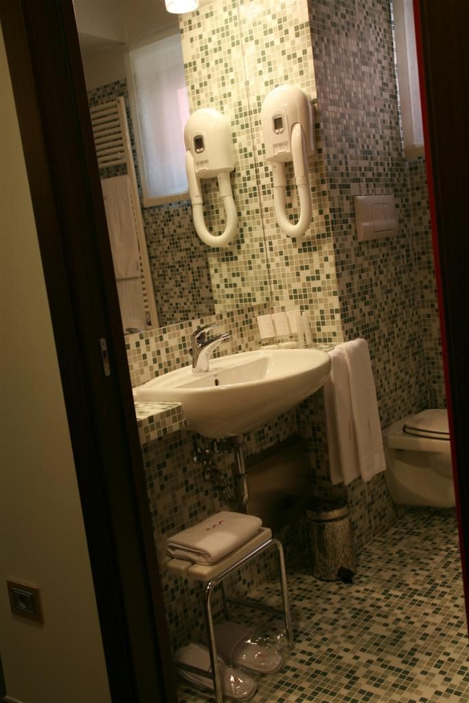 Un baño con lavamanos, dos dispensadores de toallas, inodoro y un pequeño cubo de basura.