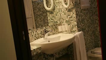 A bathroom with a sink, two towel dispensers, a toilet, and a small trash bin.