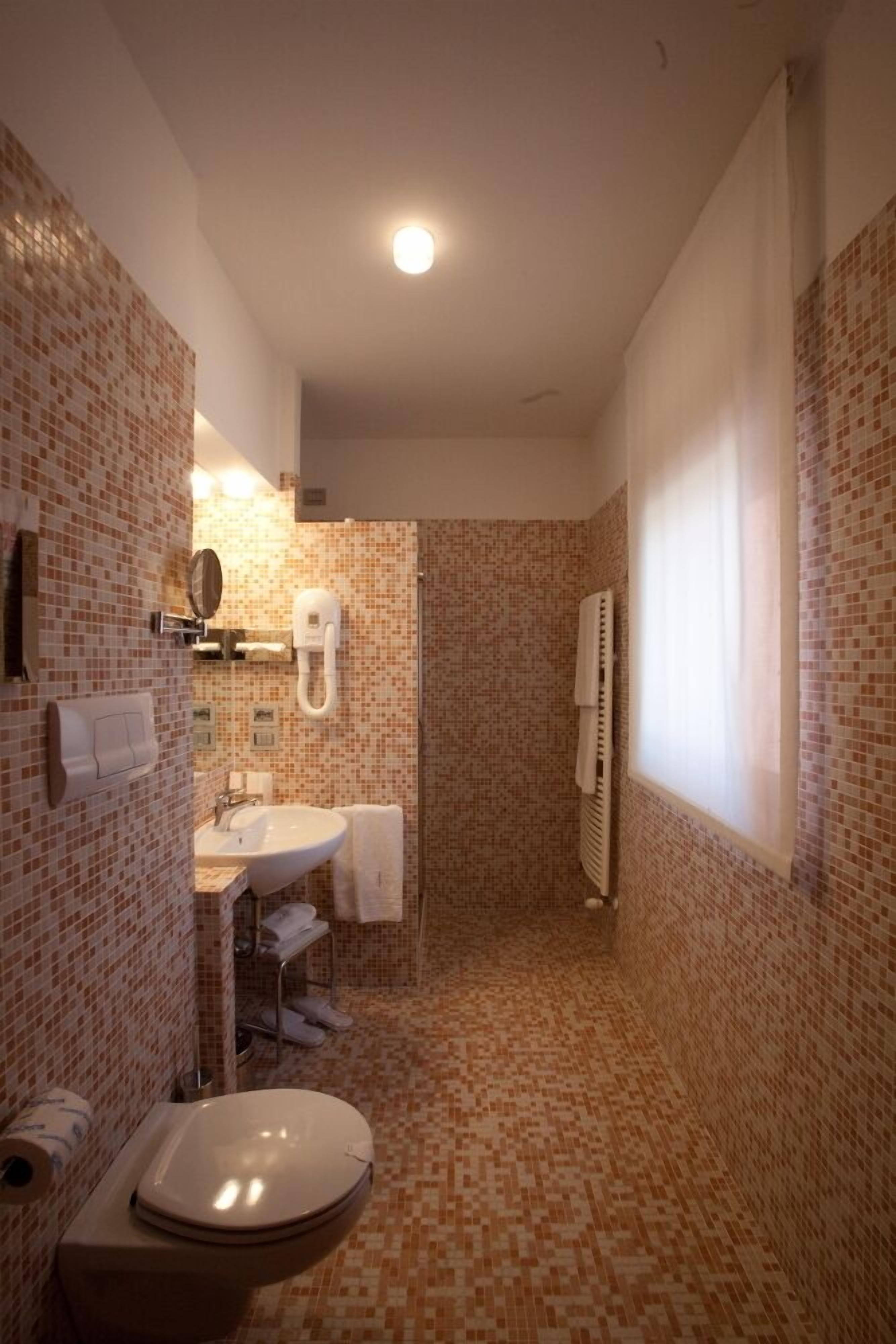 A bathroom with a tiled floor, a sink, a toilet, a mirror, and a towel rack.