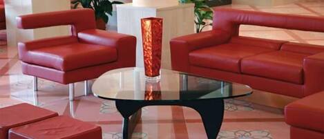 Un vestíbulo con sofás de cuero rojo, una mesa de centro de vidrio y un alto jarrón rojo.