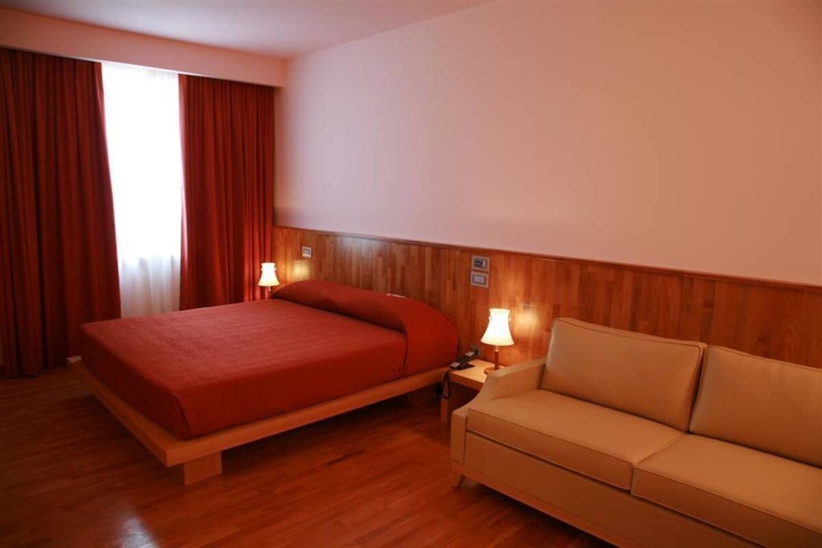 A hotel room with a wooden bed, a beige sofa, and two bedside lamps.