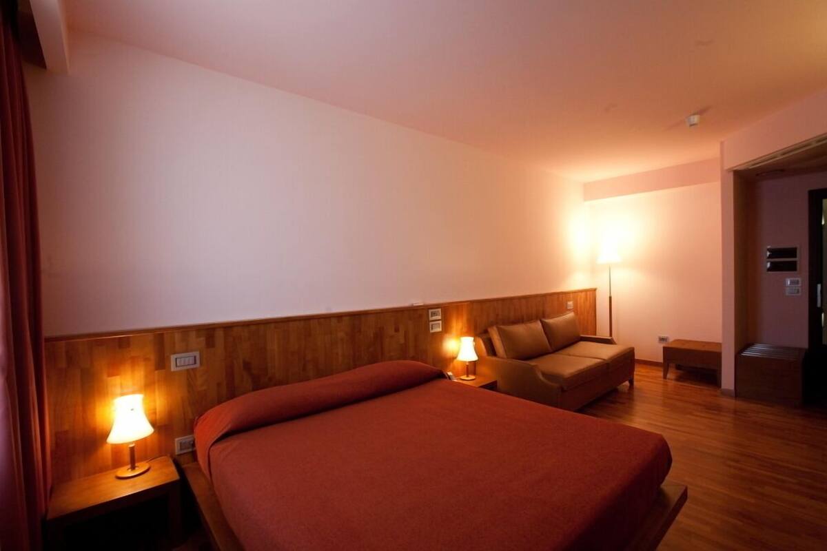 A hotel room with a large bed, two bedside lamps, a wooden headboard, a brown sofa, and a small table.