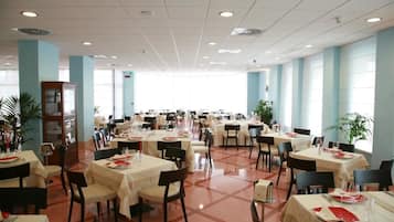 Un'ampia sala da pranzo con diversi tavoli e sedie, grandi finestre e luci a soffitto.